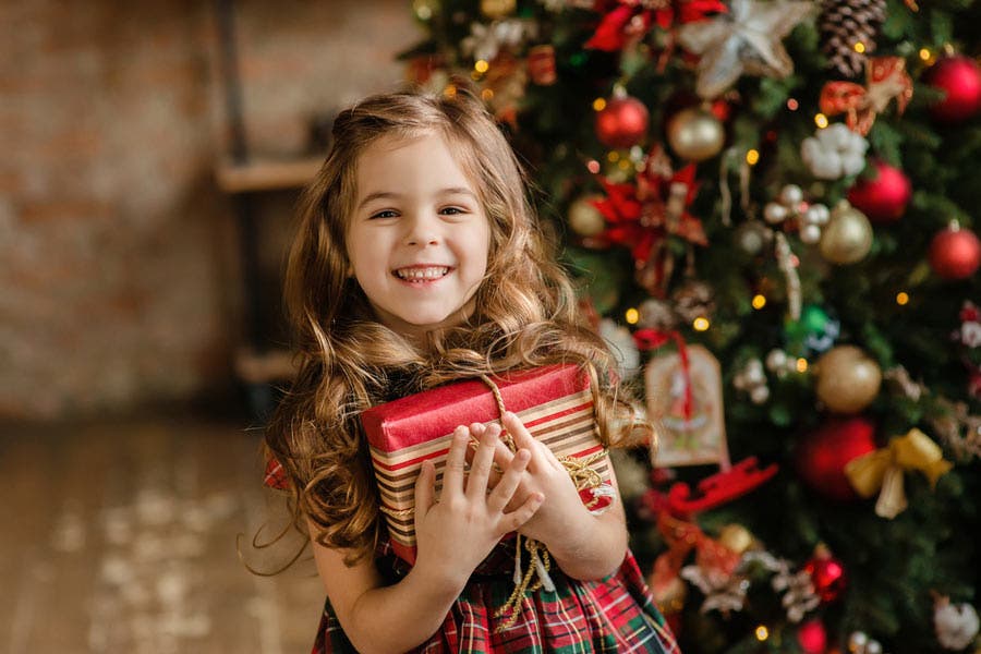 photo of a happy child holding a gift alongside the Christmas tree