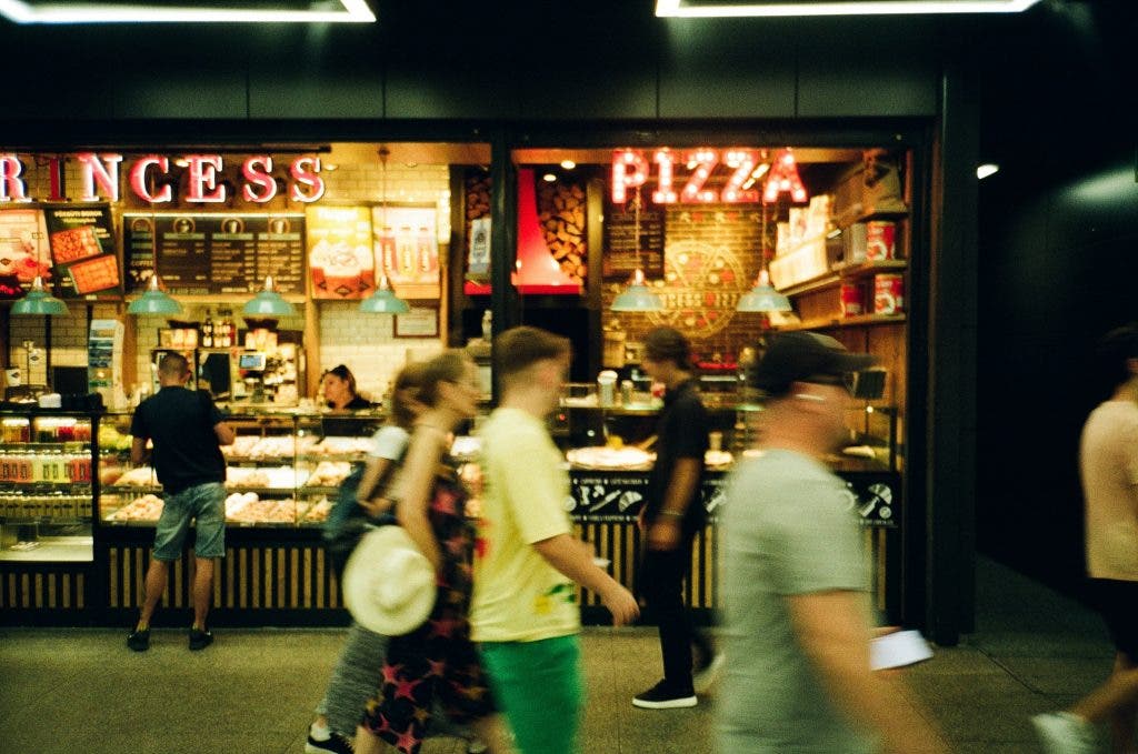 street photographer snaps a picture of people walking by a pizza place