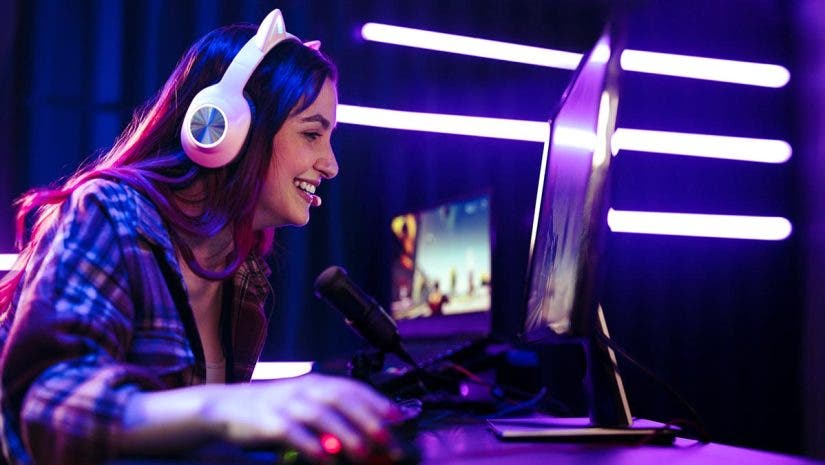 Happy young woman live streaming a video game, sitting in front of a multi monitor setup with a microphone for commentary and a headset for communication. Female engaging with fellow gamers on an online platform.